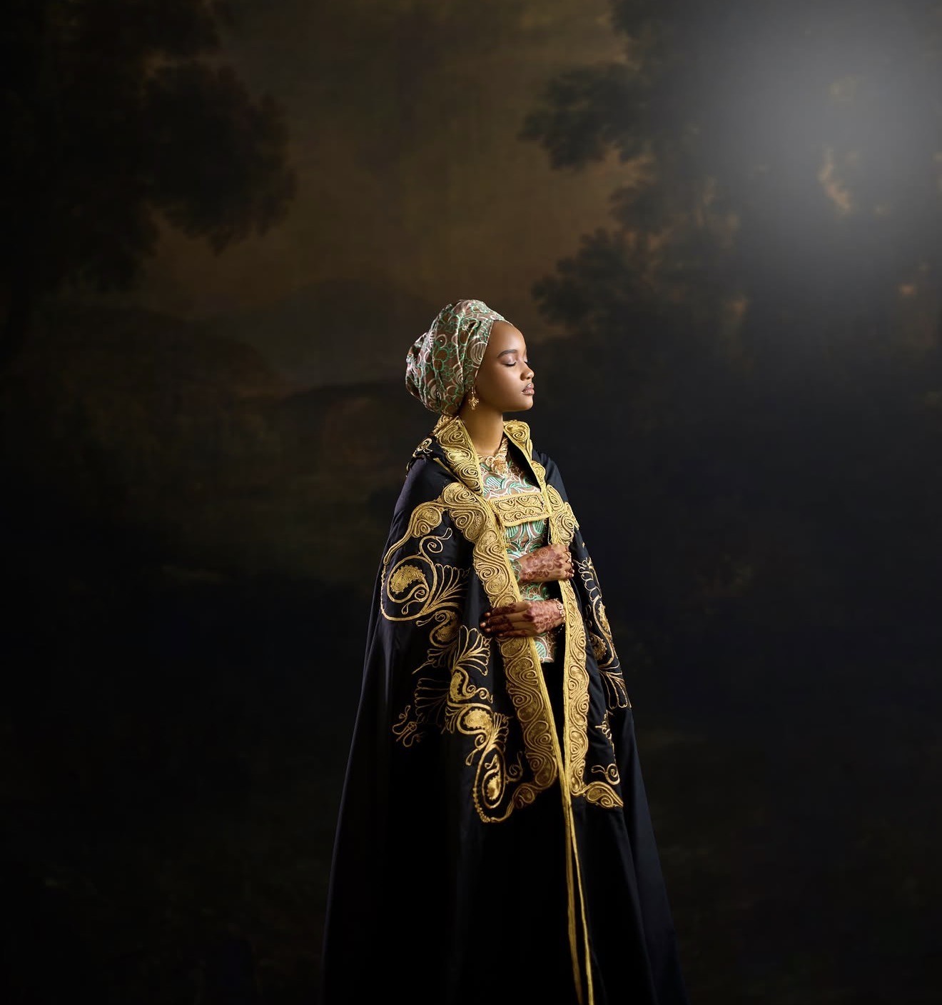 Bride in an embroidered black and gold gown against a moody painted backdrop