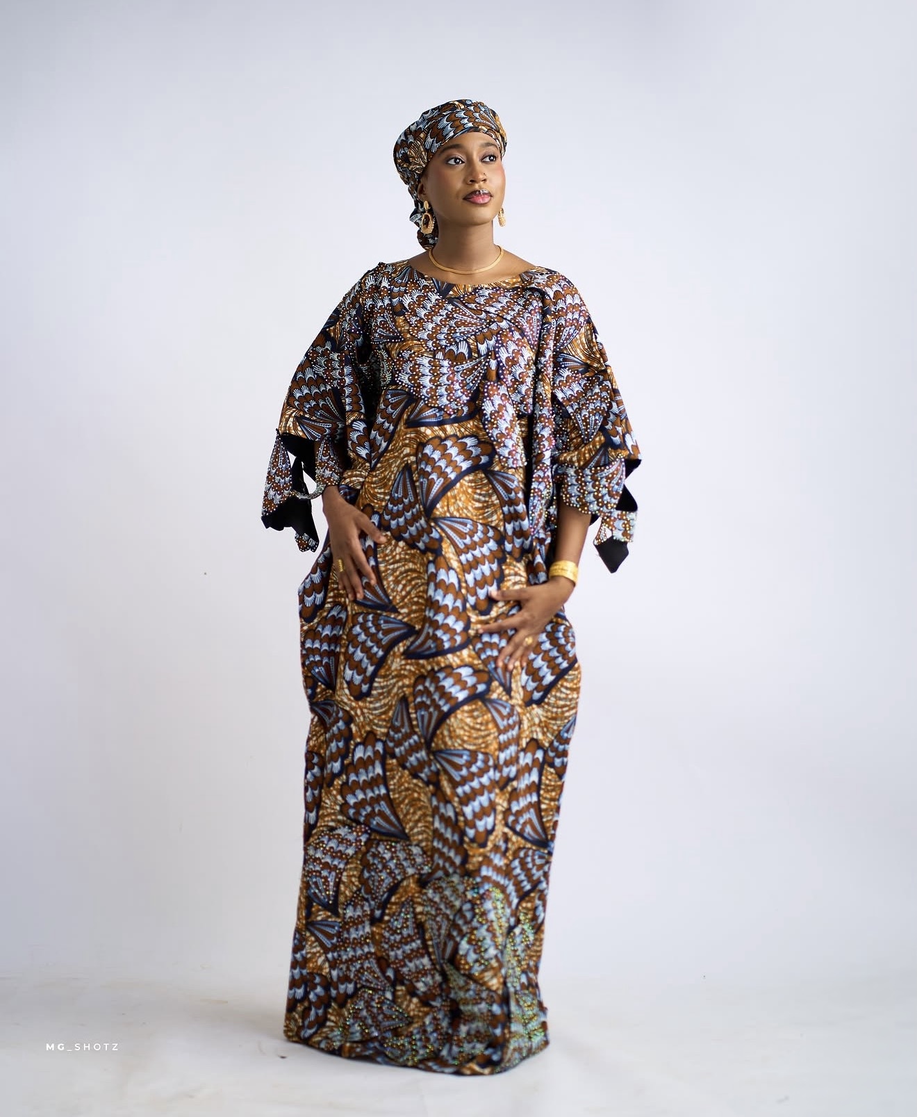 Model wearing a blue and gold patterned dress against a light studio backdrop